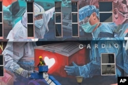 FILE - A worker adds finishing touches to giant mural tribute to frontline workers in the COVID-19 coronavirus pandemic outside a hospital in Kuala Lumpur, Malaysia, on Jan. 21, 2021.