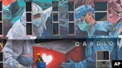 Seorang pekerja menambahkan sentuhan akhir pada mural raksasa untuk para pekerja garis depan dalam pandemi virus corona COVID-19 di luar rumah sakit di Kuala Lumpur, Malaysia, pada Kamis, 21 Januari 2021. (Foto: AP)