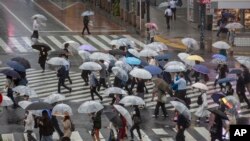 Warga Jepang menggunakan payung berjalan di penyeberangan saat Topan Mindulle bergerak di lepas pantai Jepang Jumat, 1 Oktober 2021, di Tokyo. (Foto: AP/Kiichiro Sato)