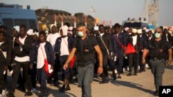 FILE - Italian border police officers escort sub Saharan men on their way to a relocation center, after arriving aboard the Golfo Azzurro rescue vessel at the port of Augusta, in Sicily, Italy.