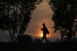 A man wearing a face mask walks at sunset in a park in Wuhan, in China's central Hubei province on April 19, 2020.