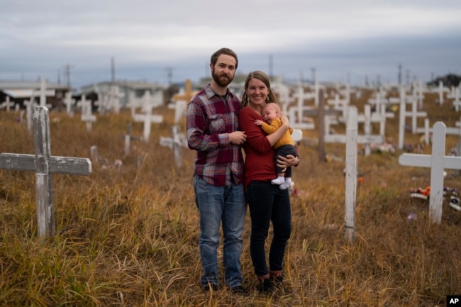 The Rev. Aaron Silco, and his wife, Anna, who are pastors at the Shishmaref Lutheran Church, stand for a photo with their two-month-old son, Aidan, in a cemetery next to the church in Shishmaref, Alaska, Tuesday, Oct. 4, 2022. (AP Photo/Jae C. Hong)
