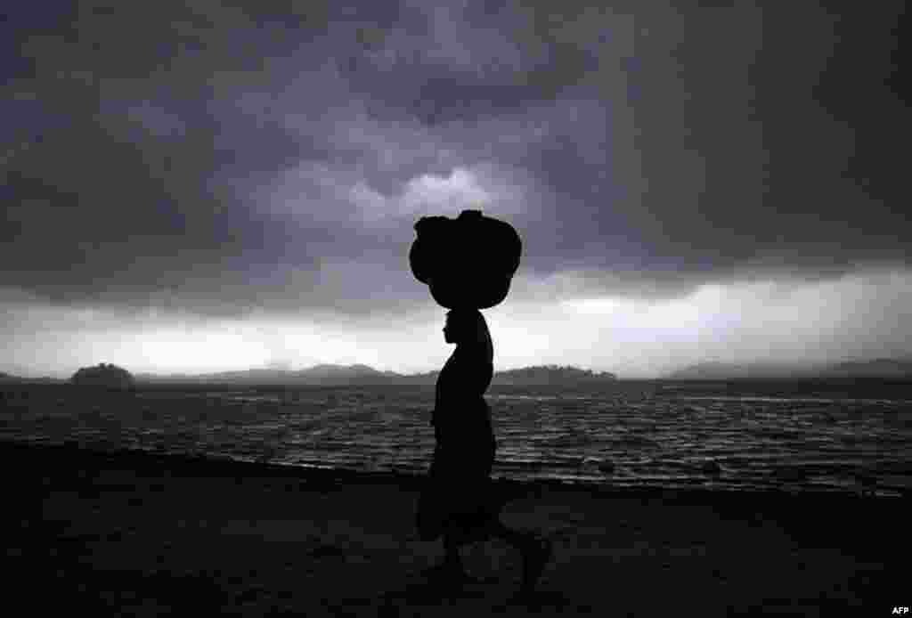 April 14: A woman carries a bundle of clothes during a thunder storm on the banks of the River Brahmaputra in Gauhati, India. (AP Photo/Anupam Nath)