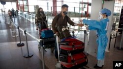 Wall Street Journal reporter Stu Woo, right, has his temperature checked while colleague Julie Wernau waits as they arrive for their departure at Beijing Capital International Airport during expulsion from China.