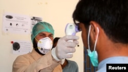 FILE - A health worker takes the temperature of a man who returned from Iran and is under medical observation, at the border post in Taftan, Pakistan, Feb. 25, 2020.