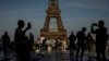 Люди зі смартфонами на тлі Ейфелевої вежі в Парижі, 7 червня 2024. AP Photo/Aurelien Morissard