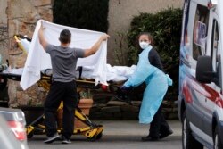 A staff member blocks the view as a person is taken by a stretcher to a waiting ambulance from a nursing facility where more than 50 people are sick and being tested for the COVID-19 virus, Feb. 29, 2020, in Kirkland, Wash.