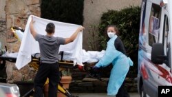 A staff member blocks the view as a person is taken by a stretcher to a waiting ambulance from a nursing facility where more than 50 people are sick and being tested for the COVID-19 virus, Feb. 29, 2020, in Kirkland, Wash. 