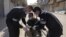 Des agents de santé aident un homme en fauteuil roulant à enfiler ses gants pour empêcher la propagation du coronavirus à Qamishli, Syrie, le 23 mars 2020.