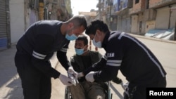 Health workers put gloves on a man in a wheelchair on an empty street, as restrictions are imposed to prevent the spread of the coronavirus in Qamishli, Syria, March 23, 2020. 