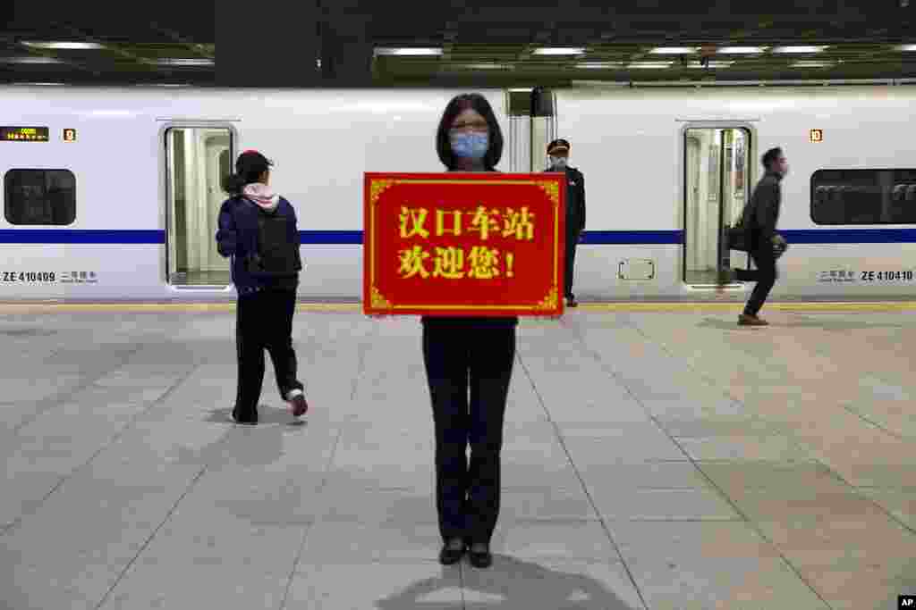 Un trabajador ferroviario sostiene un cartel que dice &quot;&iexcl;La estación Hankou te da la bienvenida!&quot; mientras los pasajeros abordan el primer tren de alta velocidad que sale de la estación de tren de Hankou después de la reanudación de los servicios de trenes en Wuhan.