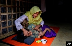 In this photograph taken Aug. 28, 2018, a Rohingya woman Ali Nesa, tends to her sick daughter inside their makeshift shelter in Kutupalong refugee camp, Bangladesh.