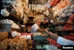 FILE - A vendor exchanges money with a customer at a shop selling garlic, onions and potatoes at a wholesale market in Mumbai, April 28, 2011. India's farmers are suffering low prices for potatoes and onions, but middle men and consumers are unaffected.
