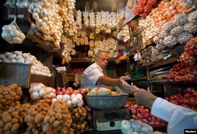 FILE - A vendor exchanges money with a customer at a shop selling garlic, onions and potatoes at a wholesale market in Mumbai, April 28, 2011. India's farmers are suffering low prices for potatoes and onions, but middle men and consumers are unaffected.