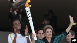 Brazil’s President Dilma Rousseff, right, waves for people next to Olimpic Athlete Fabiana Claudino, during lighting ceremony of torch with the Olympic flame at Planalto Presidential Palace, in Brasilia, Brazil,Tuesday, May 3, 2016.