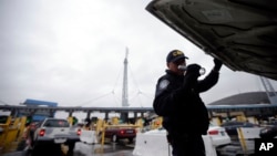 FILE - A U.S. Customs and Border Protection (CBP) officer checks under the hood of a car as it waits to enter the U.S. from Tijuana, Mexico through the San Ysidro port of entry in San Diego, Dec. 3, 2014.