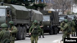 Armed servicemen wait near Russian army vehicles outside a Ukrainian border guard post in the Crimean town of Balaclava, March 1, 2014. 