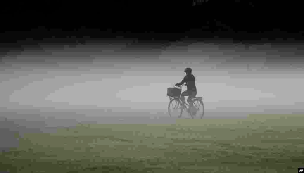 A woman rides her bicycle through a heavy mist in a park as the sun rises in Sydney, Australia.