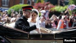 Pangeran Harry dan istrinya, Meghan Markle, melambaikan tangan ke arah pengunjung saat mengendarai kereta kuda setelah upacara pernikahan di Kapel St. George di Windsor, Inggris, 19 Mei 2018. 