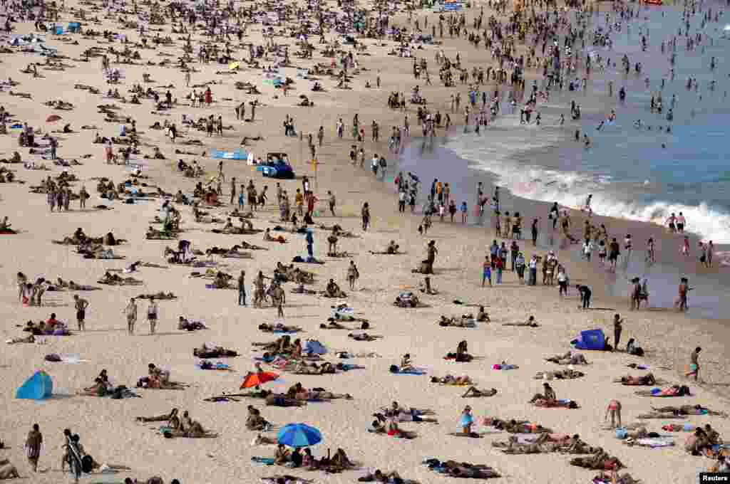 Beachgoers swim and sit on Bondi beach during a hot spring day in Sydney, Australia.