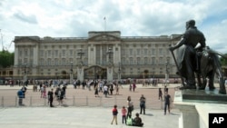 FILE - People are seen in front of Britain's Queen Elizabeth II's official London residence, Buckingham Palace, in London.