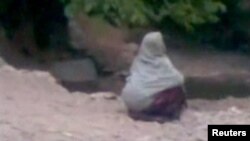 A woman accused of adultery squats in front of a crowd before her public execution by a man who Afghan officials say is a member of the Taliban, in a village outside Kabul in this still image taken from undated footage released July 7, 2012.