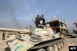 FILE - Iraqi Shiite fighters from the Popular Mobilisation units, fighting alongside Iraqi government forces, display, upside down, the flag of the Islamic State (IS) group during a military operation aimed at the centre of Baiji, Iraq, Oct. 19, 2015.