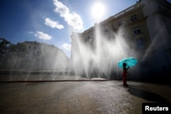 A girl uses an umbrella to play near a water sprinkler in the hot weather in Vienna, Austria, July 23, 2019. (Photo: Reuters)