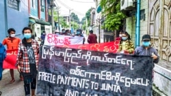 In this photo provided by Mandalay Strike Force, protesters walk through the city of Mandalay in Myanmar on Oct. 28, 2021, with signs reading 'Freeze Payments to Junta.'