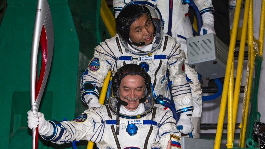 El cosmonauta ruso Mikhail Tyurin sostiene la antorcha Olímpica antes de ingresar al cohete Soyuz, acompañado por el astronauta japonés Koichi Wakata.