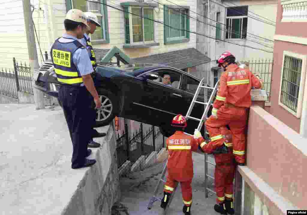 Rescue workers try to help a driver out of his car, after the vehicle was stuck over an alley in Wenzhou, Zhejiang province, Aug. 4, 2014. The car rolled off the edge of a road after the driver was late to brake, according to local media.