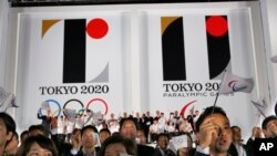 Visitors wave flags in front of the official emblems of the Tokyo 2020 Olympics and Paralympic Games at Tokyo Metropolitan Plaza in Tokyo, July 24, 2015..