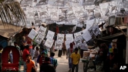 People walk near posters with portraits of contesting candidates urging voters to cast their ballot for their respective parties hung overhead on a street in Dhaka, Bangladesh, Jan. 3, 2014. 