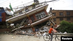 A boy riding a bicycle looks at a collapsed house after Saturday's earthquake, in Kathmandu, Nepal, April 28, 2015. 