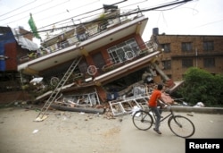 A boy riding a bicycle looks at a collapsed house after Saturday's earthquake, in Kathmandu, Nepal, April 28, 2015.