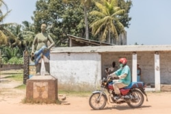 Un homme à moto passe devant le statut devant la place commémorative Zomachi à Ouidah le 4 août 2020.