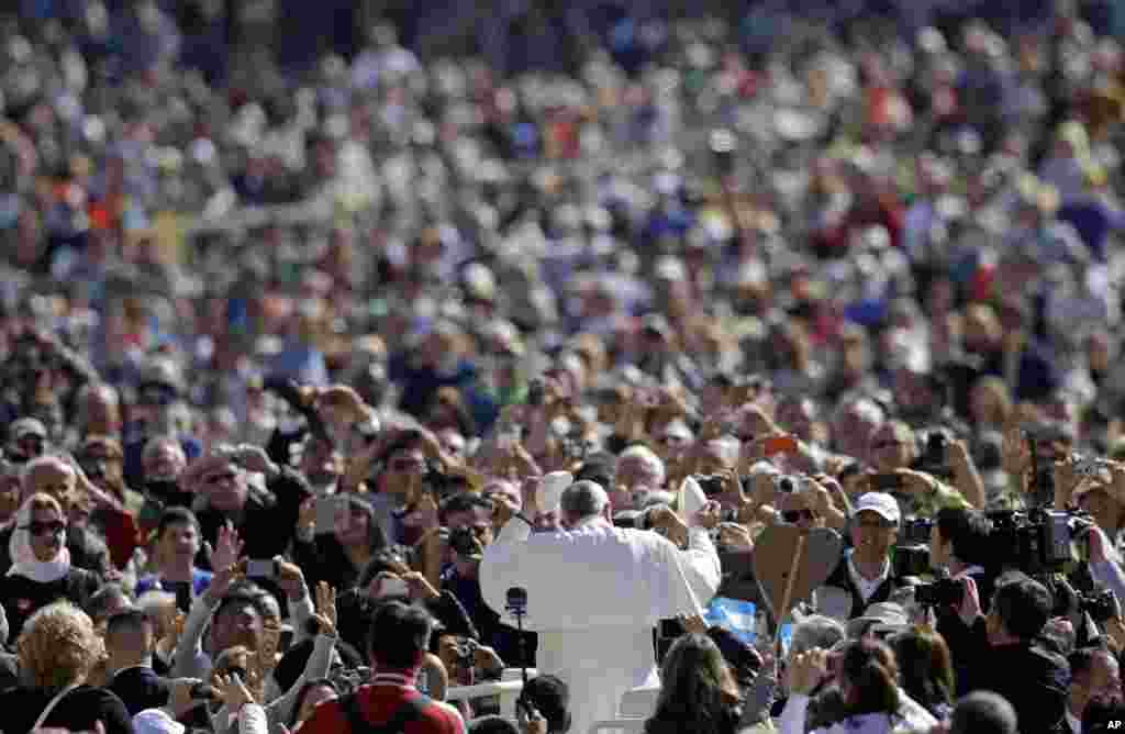 Paus Fransiskus, tengah, mengganti topinya dengan topi yang diberikan oleh seorang peziarah ketika ia tiba untuk menyampaikan khotbah mingguannya di Lapangan Santo Petrus di Vatikan.