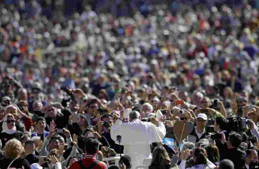 Pope Francis, center, exchanges his skull cap with one donated to him by a pilgrim as he arrives for his weekly general audience, in St. Peter's Square at the Vatican.