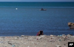 FILE - A woman defecates along the shoreline in Cite Soleil slum, in Port-au-Prince, Haiti, Dec. 25, 2016.