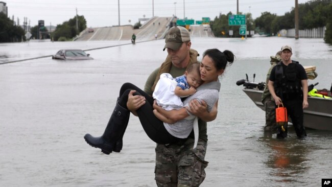 Houston Police SWAT officer Daryl Hudeck carries Catherine Pham and her 13-month-old son Aiden after rescuing them from their home surrounded by floodwaters from Tropical Storm Harvey Sunday, Aug. 27, 2017, in Houston.