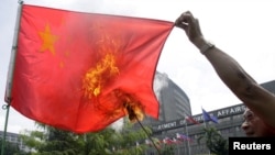 Một người biểu tình đốt cờ Trung Quốc ở Manila. Hà Nội dường như dang rộng vòng tay với với các quốc gia khác cùng chí hướng như Philippines nhằm ngăn chặn sự lấn lướt của Bắc Kinh trên biển Đông.