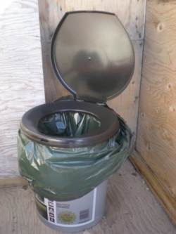 An indoor "honey bucket," a plastic bucket fitted with a toilet seat for comfort and a plastic bag for waste containment.