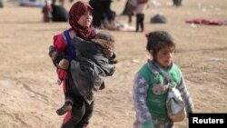 A girl walks as she holds a child near Baghuz, Deir el-Zour province, Syria, March 5, 2019.