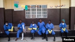 Le personnel de santé assis devant une maison dans une zone de quarantaine dnas les instatallations de la Croix Rouge au village de Koidu, district de Kono, dans l'est de la Sierra Leone, le 19 décembre 2014.