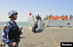 FILE - A navy soldier in the People’s Liberation Army stands guard as Chinese citizens board the naval ship ‘Linyi’ at a port in Aden.