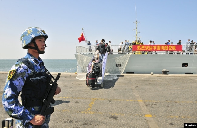 FILE - A navy soldier in the People’s Liberation Army stands guard as Chinese citizens board the naval ship ‘Linyi’ at a port in Aden.