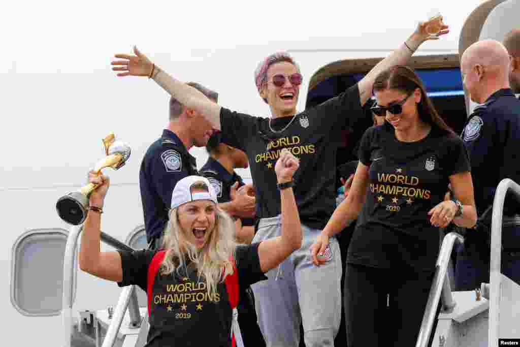 U.S. soccer players Julie Ertz (L), Megan Rapinoe (C) and Alex Morgan celebrate as they exit the plane with the Trophy for the FIFA Women's World Cup as the team arrives at the Newark International Airport, in Newark, New Jersey, July 08, 2019.