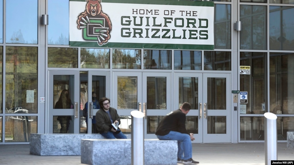 Students sit outside the entrance to Guilford High School with a sign of the new representative for the school that replaced an image of Indians on Tuesday, Oct. 19, 2021, in Guilford, Conn. (AP Photo/Jessica Hill)