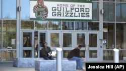 Students sit outside the entrance to Guilford High School with a sign of the new representative for the school that replaced an image of Indians on Tuesday, Oct. 19, 2021, in Guilford, Conn. (AP Photo/Jessica Hill)