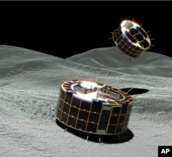 This computer graphic image provided by the Japan Aerospace Exploration Agency (JAXA) shows two drum-shaped and solar-powered Minerva-II-1 rovers on an asteroid. (JAXA via AP)